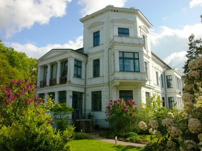 Ein zweigeschossiger Putzbau in Richtung Friedenstraße mit vorspringendem um ein Geschoss erhöhtem dominanten Bauteil. 